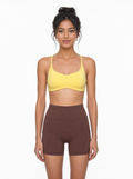 Woman wearing a yellow sports bra and brown shorts on a white background