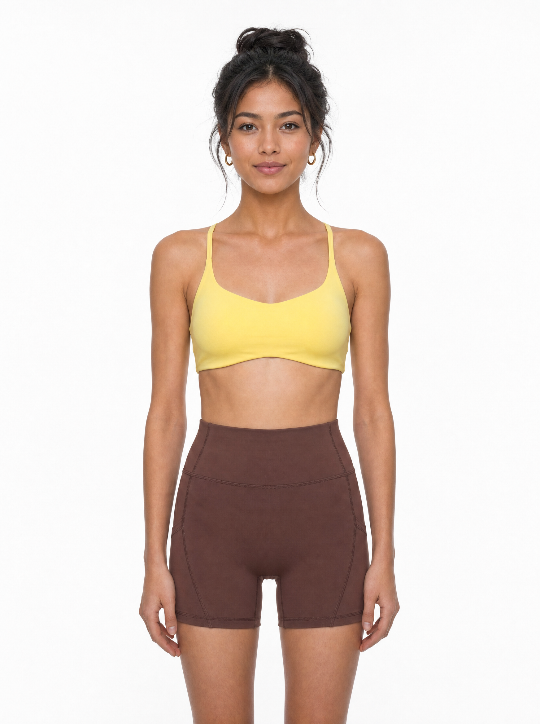 Woman wearing a yellow sports bra and brown shorts on a white background